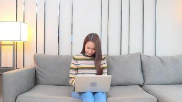 Young asian woman uses a laptop on the couch video