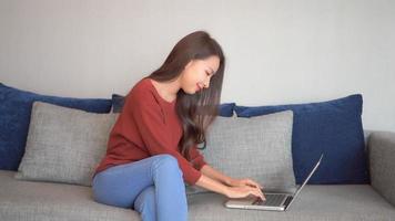 Joven mujer asiática usa una computadora portátil en el sofá
