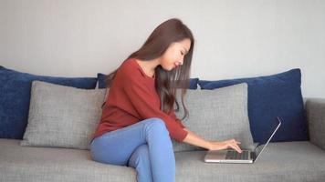 Joven mujer asiática usa una computadora portátil en el sofá