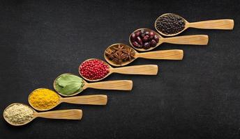 Spices in spoons over black table background photo