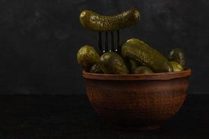 Gherkins and sauerkraut in a clay bowl on a dark concrete background photo