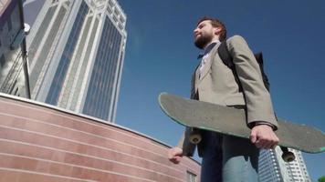 Jeune homme d'affaires barbu ride sur skateboard en plein air video