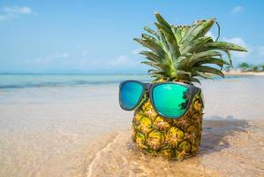 Pineapple with sunglasses on tropical beach background. Summer concept