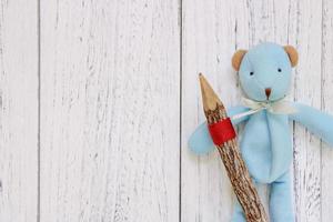 mesa de madera pintada de blanco muñeca de oso azul sosteniendo un lápiz foto