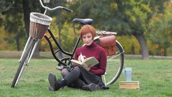 jovem mulher com livro e bicicleta no parque