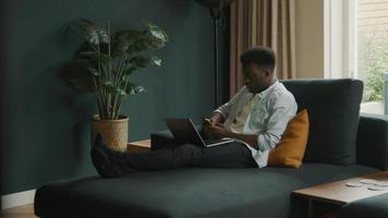 hombre sentado en el sofá con la computadora portátil escribiendo en el teléfono inteligente l video