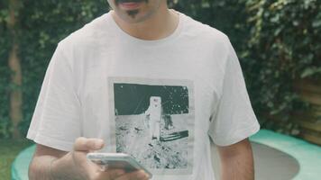 Man standing in garden typing on smartphone looking up into lens video