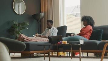 homem lendo livro e mulher sentada na sala de estar usando o controle remoto video