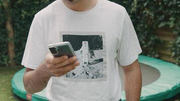 Man standing in garden typing on smartphone looking up into lens video