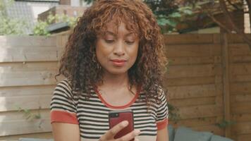 Woman standing in garden watching smartphone looks up into lens video