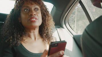 Woman sitting in back of car talks and looks at smartphone video