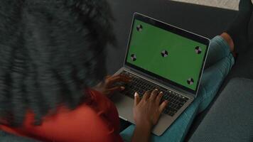 Woman sitting on sofa typing on laptop with green screen video