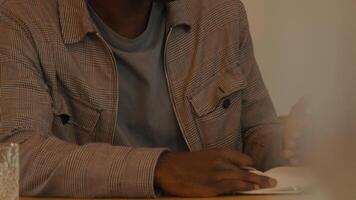 Man sitting at table with notebook talking whilst person walks by video