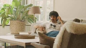 Man lying on sofa putting on headphone and moving head video