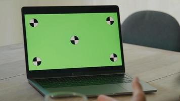 Close up of laptop with green screen on table and two people in front video
