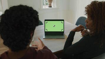 Woman and man at table having conversation with green screen laptop video