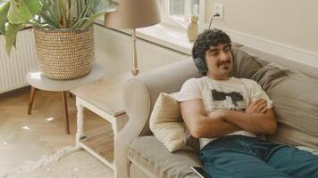 Man with headphone lying on sofa moves head on rhythm looking happy video