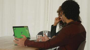 Woman and man at table having conversation with green screen laptop video