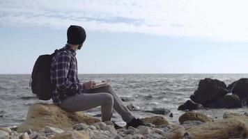 junger männlicher Reisender mit Buch am Strand mit Rucksack video