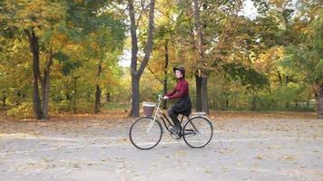 giovane donna in sella a una bicicletta retrò nel parco autunnale video
