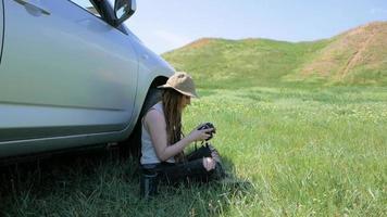 young woman traveler sitting near  offroad car with digital camera video