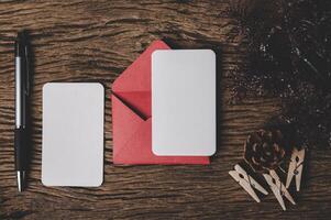 Se colocan dos tarjetas en blanco con sobre rojo y bolígrafo sobre madera. foto