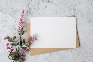 Se coloca una tarjeta en blanco con sobre y flor sobre fondo blanco. foto