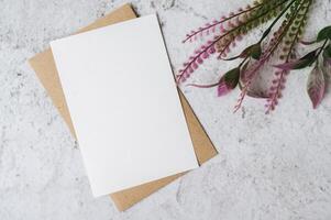 Se coloca una tarjeta en blanco con sobre y flor sobre fondo blanco. foto