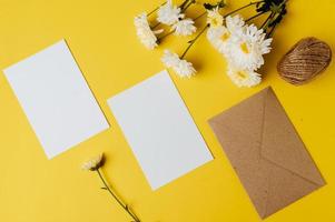 Se coloca una tarjeta en blanco con sobre y flor sobre fondo amarillo. foto