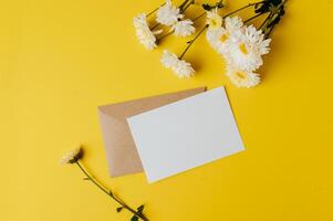 A blank card with envelope and flower is placed on yellow background photo