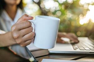 taza blanca en la mano y computadora portátil en la mesa foto