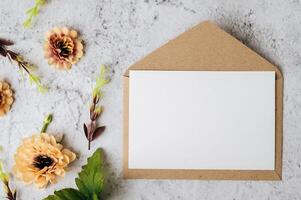 Se coloca una tarjeta en blanco con sobre y flor sobre fondo blanco. foto