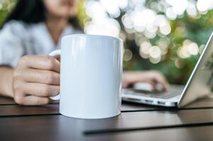 taza blanca en la mano y computadora portátil en la mesa foto