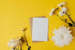 Se coloca una tarjeta en blanco con sobre y flores sobre fondo amarillo. foto