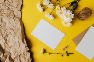 Se coloca una tarjeta en blanco con sobre y flor sobre fondo amarillo. foto