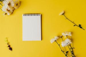 Cuaderno y flor se coloca sobre fondo amarillo. foto