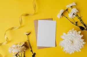 Se coloca una tarjeta en blanco con sobre y flores sobre fondo amarillo. foto