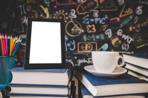 black photo frame and cup on books in classroom with colored pencils.