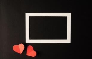White photo frame and red heart paper pasted on a black background.