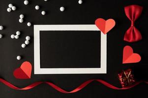 marco de fotos blanco y papel de corazón rojo pegado sobre un fondo negro.