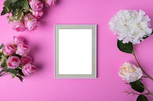 Photo frames and flowers placed on a pink background.