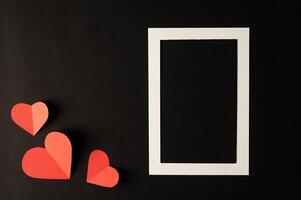 White photo frame and red heart paper pasted on a black background.