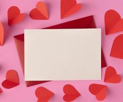 White paper and red hearts are placed on a pink background.