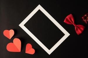 White photo frame and red heart paper pasted on a black background.