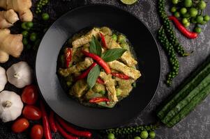 Pork green curry in black plate with spices on black cement background photo