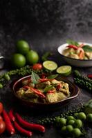 Pork green curry in a brown bowl with spices on a black cement photo