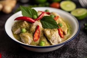 Pork green curry in a white bowl with spices on a black cement photo