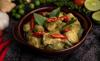 Pork green curry in a brown bowl with spices on a black cement photo