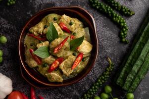 Pork green curry in a brown bowl with spices on a black cement photo