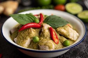 Pork green curry in a white bowl with spices on a black cement photo